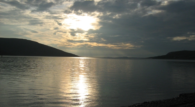 sunset over a calm flat loch broom with the sun behind light clouds and a flat loch and hills either side